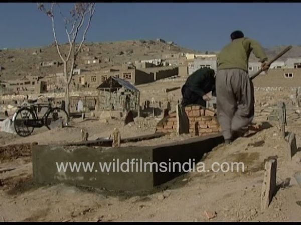 Graves and tombs being dug in Kabul Afghanistan, in 1990's. Women in blue walk walk vast landscape