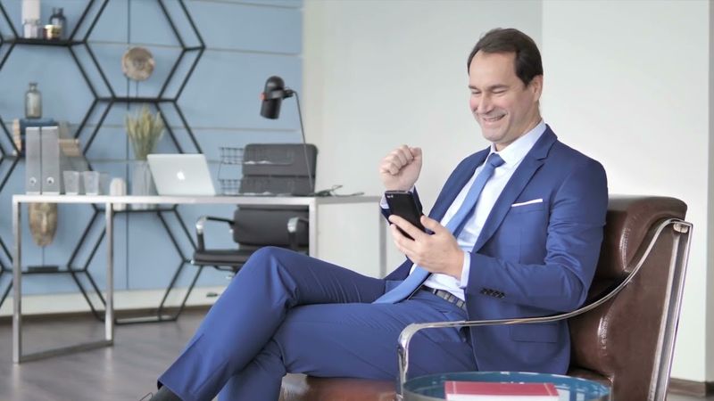 Stock Video Happy Businessman Excited for Success Using Smartphone